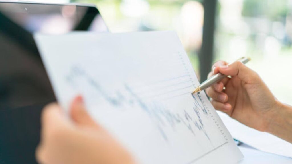Hand holding pen reviewing a financial chart on paper.